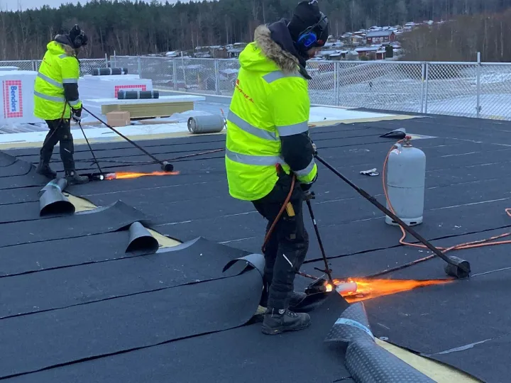 Två takläggare från Stenstorps Tak svetsar takpapp på ett platt tak